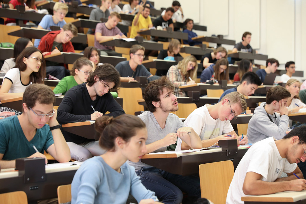 Many students sitting in a lecture theatre taking notes during a lecture.